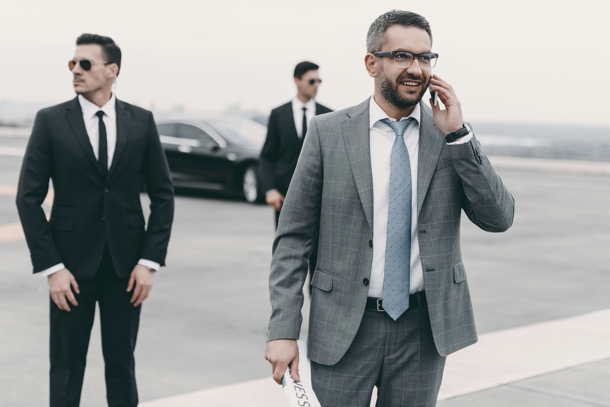 smiling-businessman-walking-with-bodyguards-and-talking-by-smartphone